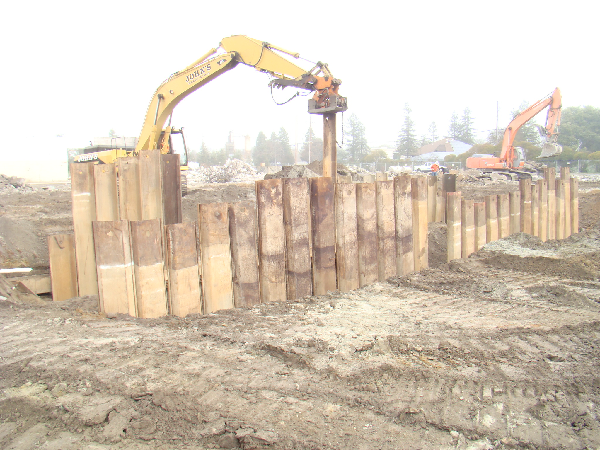 excavator placing large metal beams vertically in ground